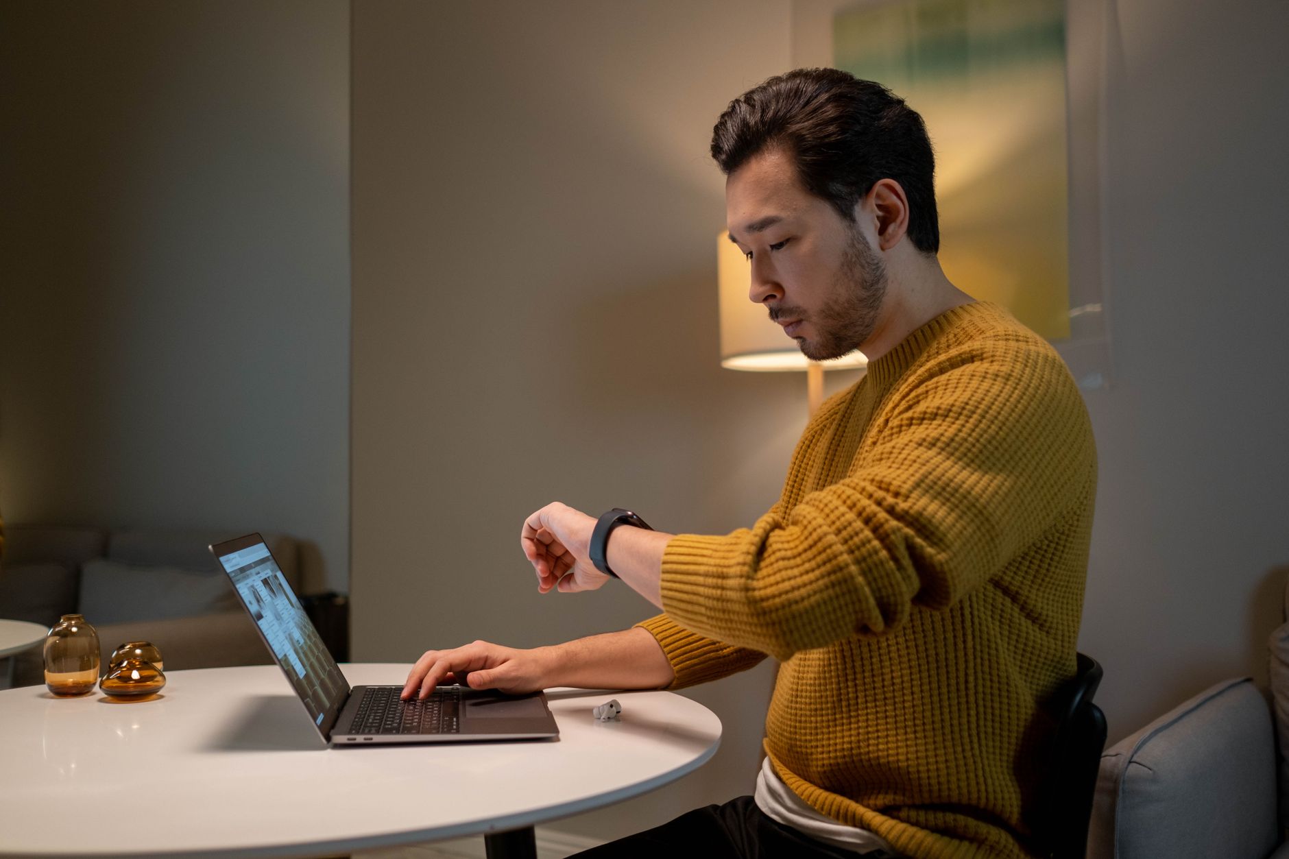 スマートウォッチで時間を確認しながらノートPCで仕事をする男性